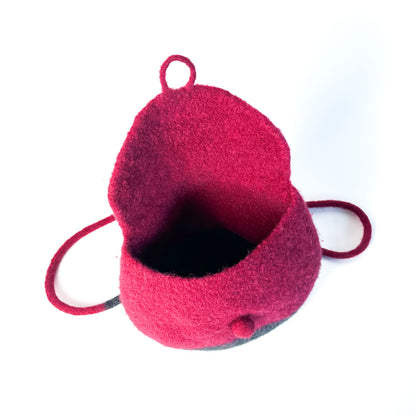 Open, two-tone felted backpack with a button detail and thin shoulder straps, showing the dark interior. The upper portion is a vibrant color.
