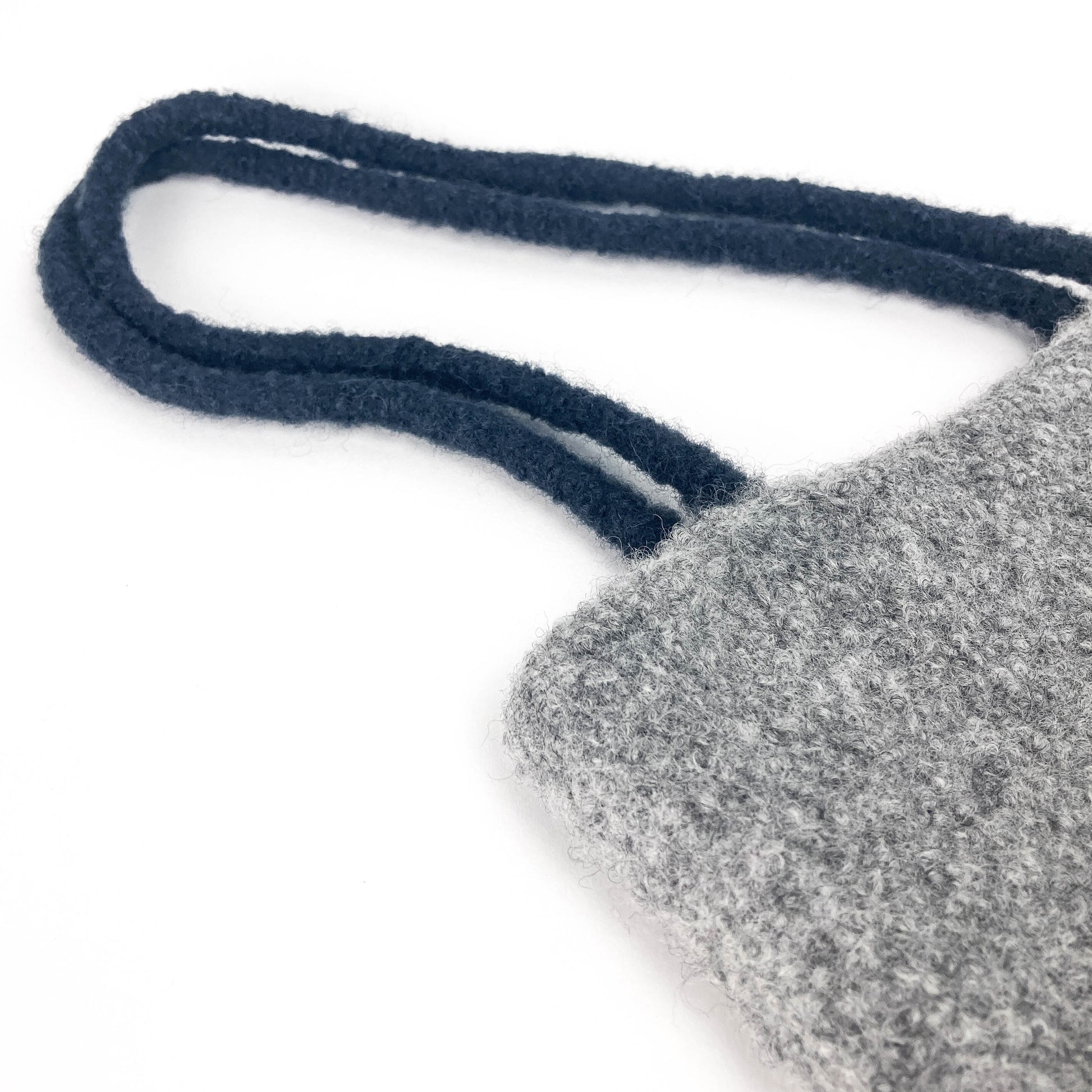 Close-up of a gray felted bag with thick, dark looped handles. The texture of the felt is visible.