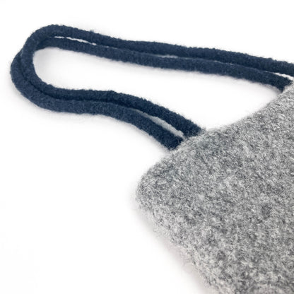 Close-up of a gray felted bag with thick, dark looped handles. The texture of the felt is visible.