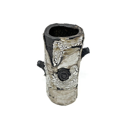 A cylindrical vase resembling birch bark with a textured surface, featuring black and white elements and two protruding branch-like details.