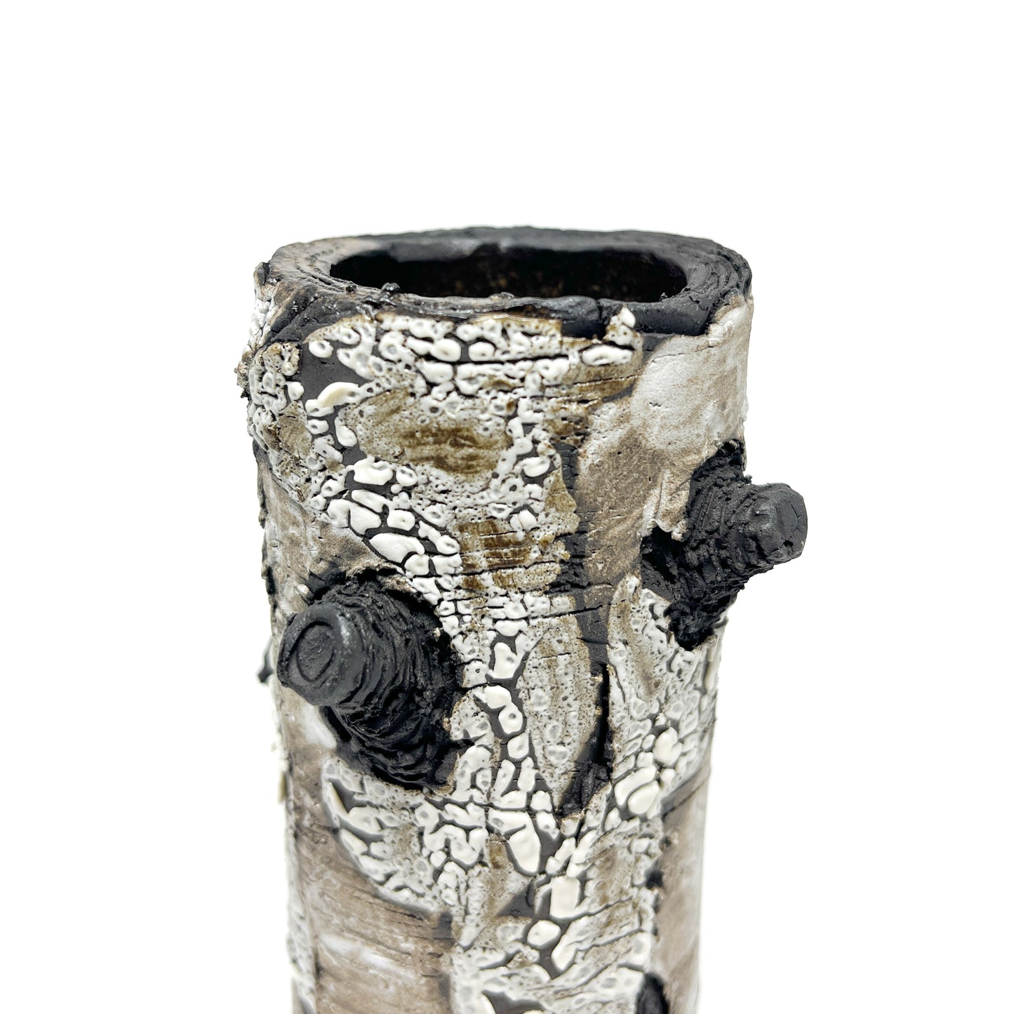 A close-up view of a cylindrical vase resembling birch bark with a textured surface, featuring black and white elements and a protruding branch-like detail.