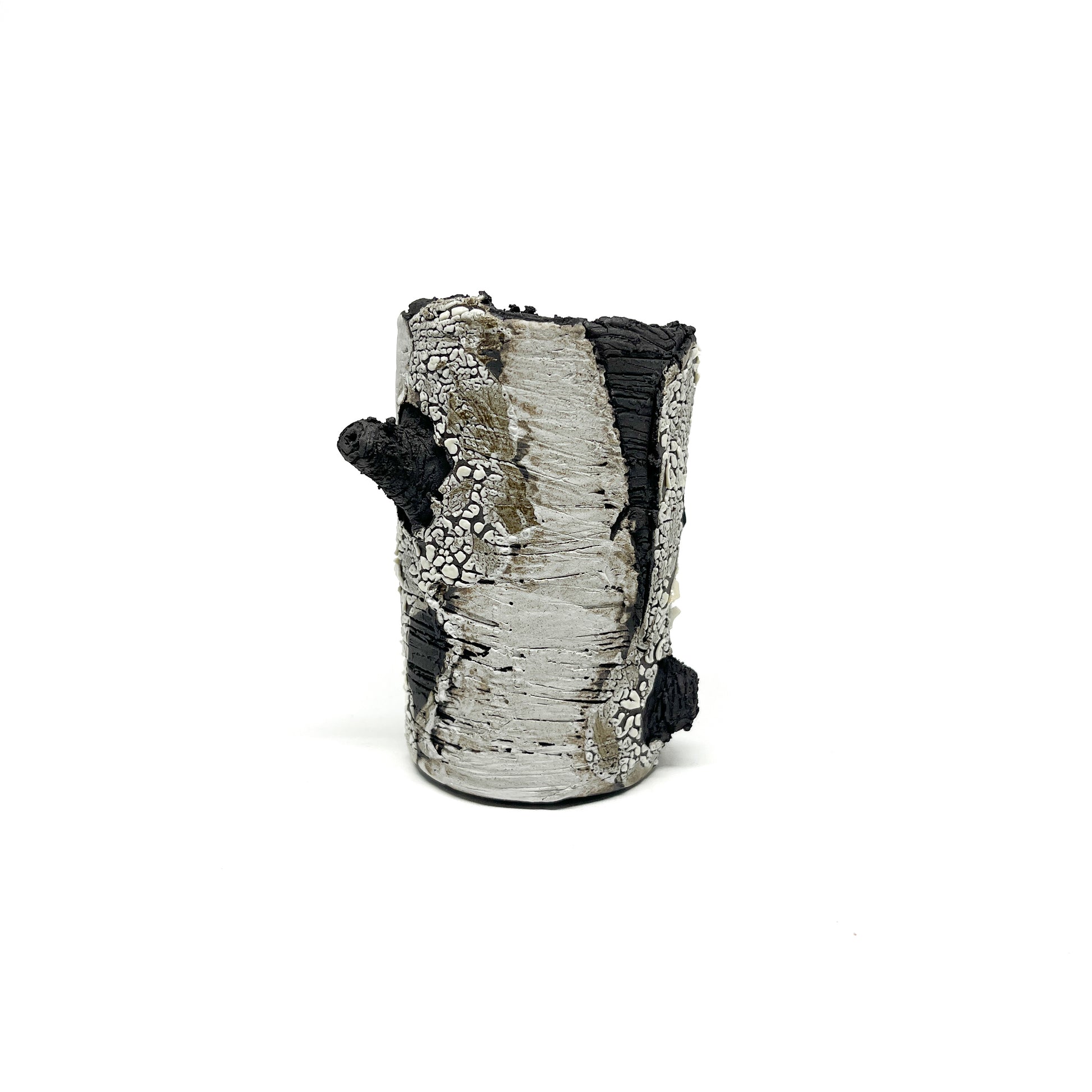 A cylindrical vase resembling birch tree bark, with black and white textured surfaces and a protruding branch-like element.