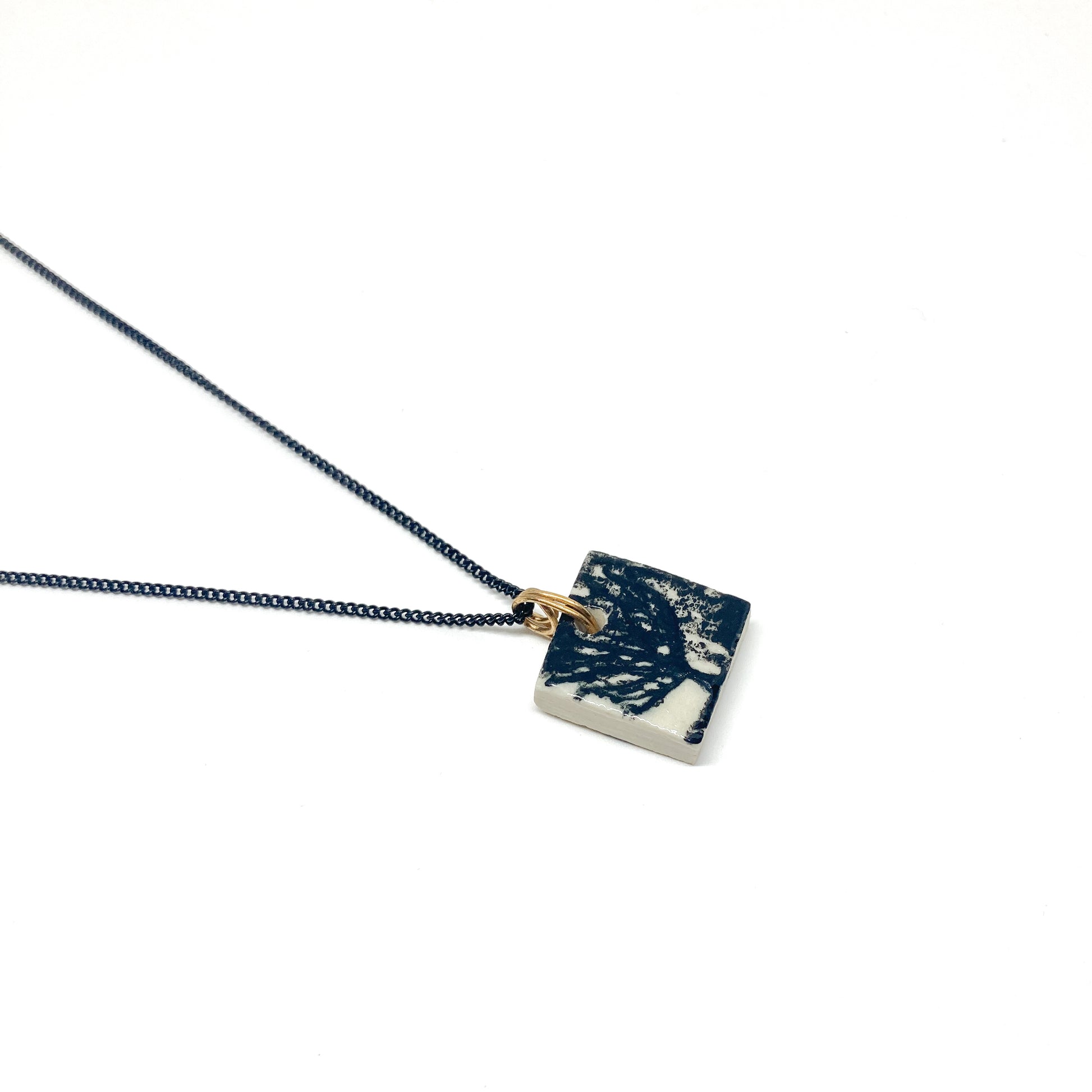 A square pendant necklace with a tree design, hanging on a thin, dark chain with a gold loop.