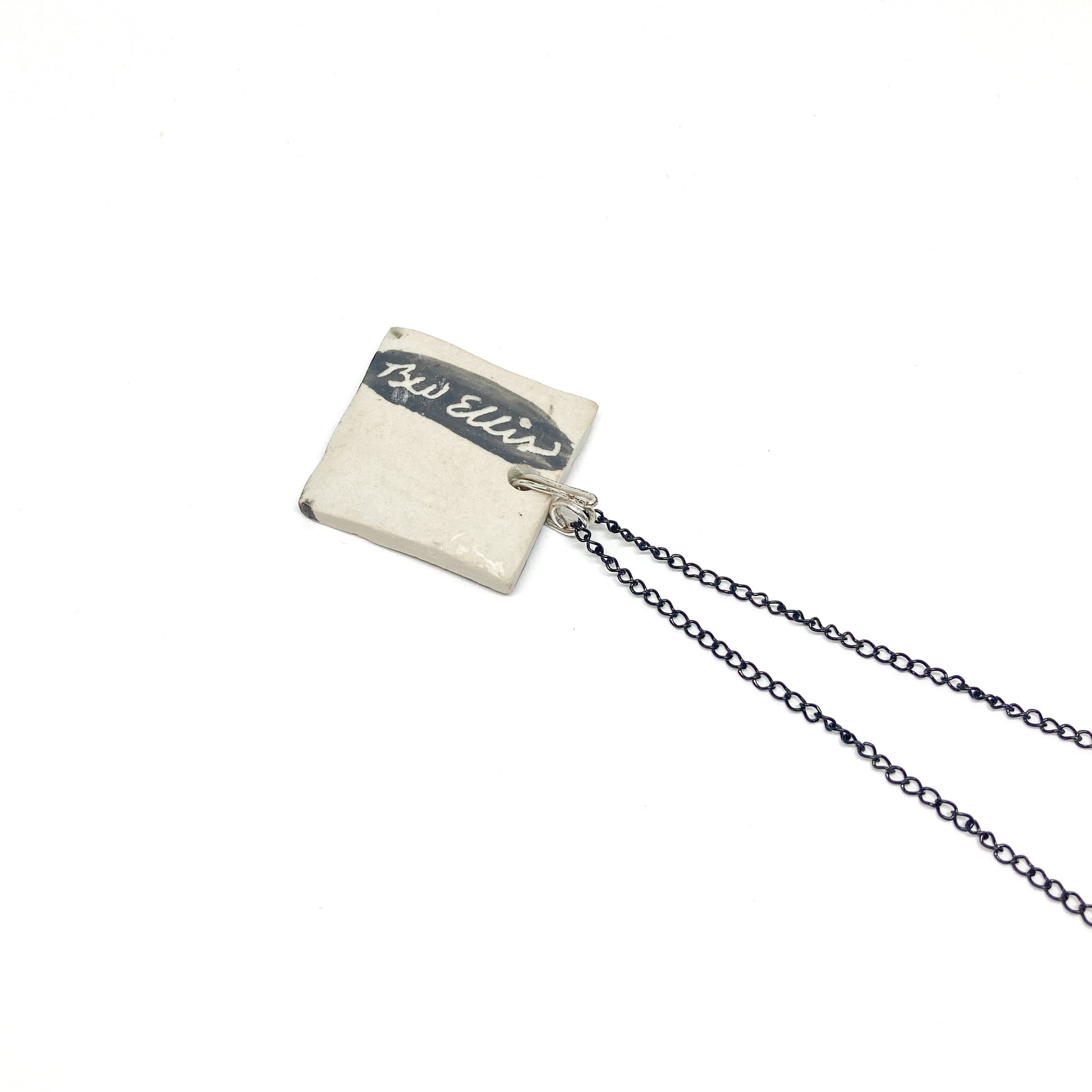 A square pendant necklace with "BW Ellis" written on it, hanging on a thin, dark chain.