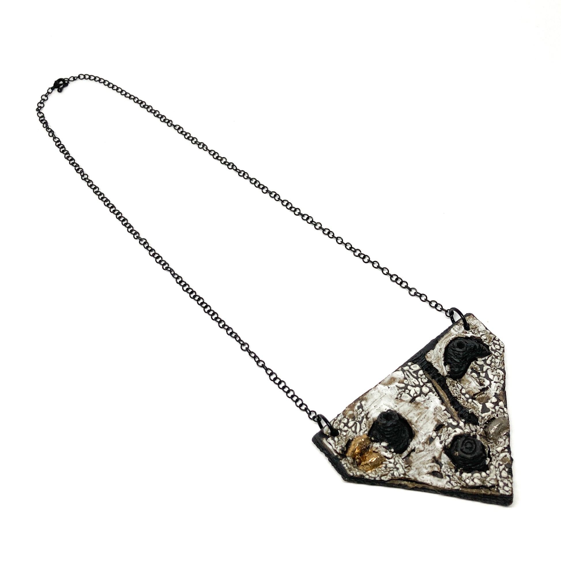Triangular pendant necklace with a textured surface, featuring black, white, gold, and silver elements, on a dark chain.