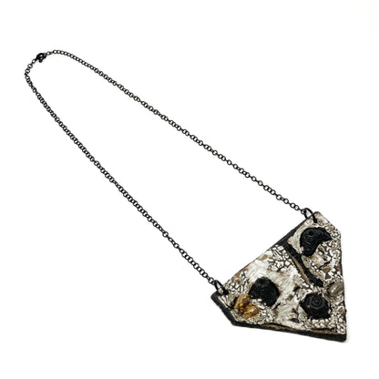 Triangular pendant necklace with a textured surface, featuring black, white, gold, and silver elements, on a dark chain.
