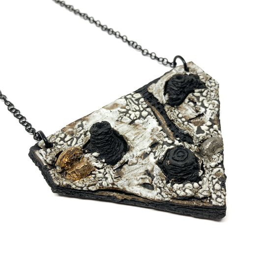 A triangular pendant necklace with textured surface, featuring black, white, gold, and silver elements.