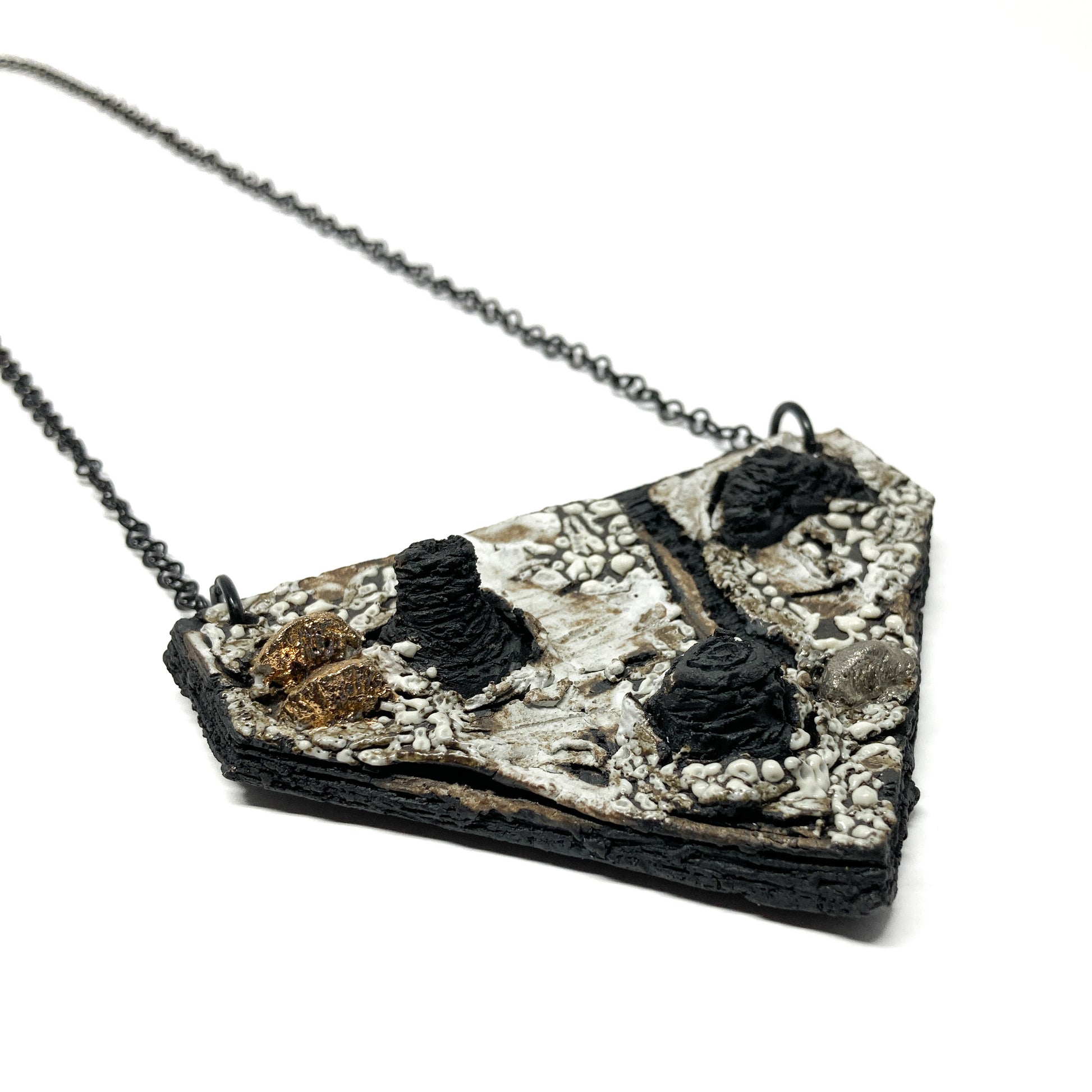 A triangular pendant necklace with a textured surface, featuring black, white, gold, and silver elements, on a dark chain.