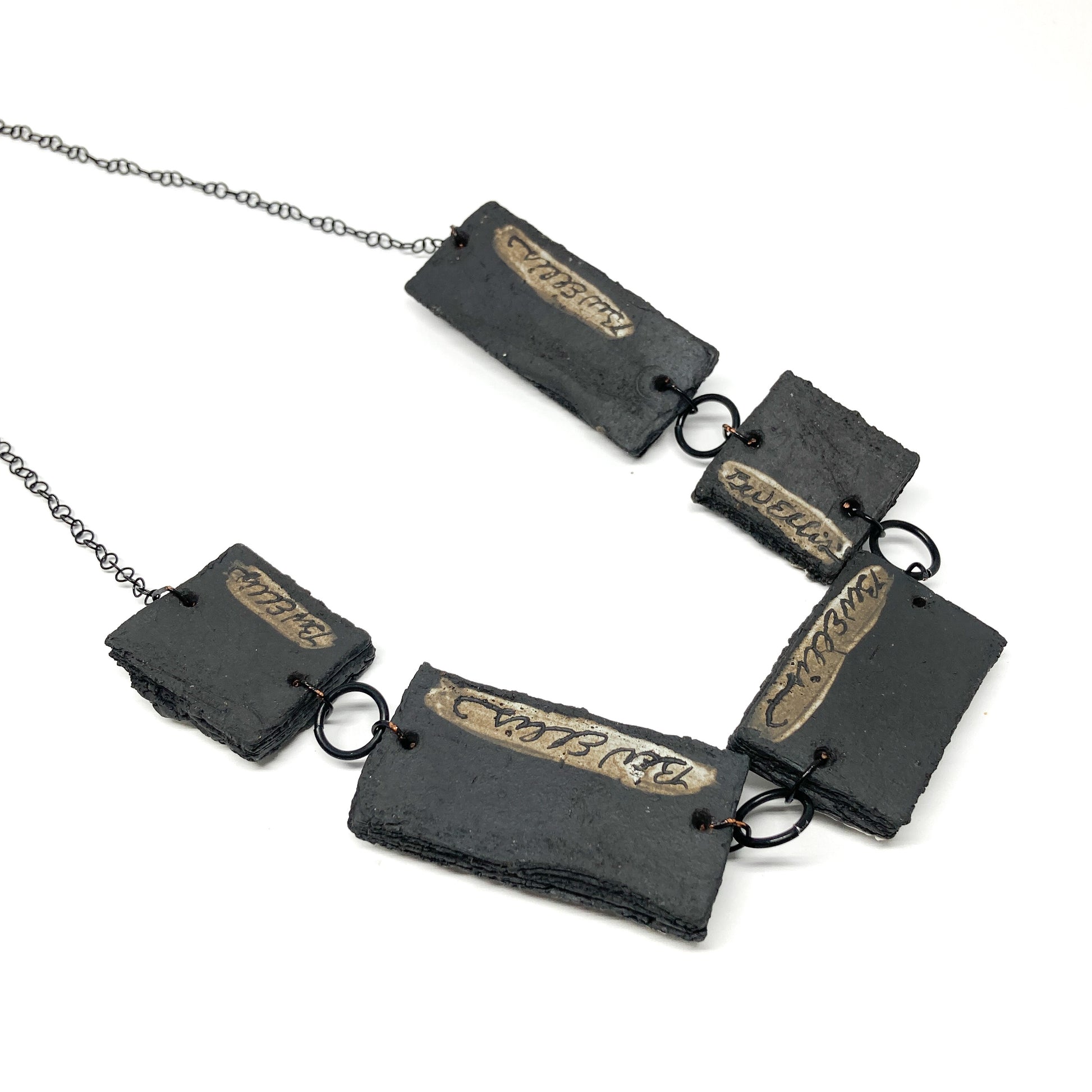 A necklace with five rectangular pendants, each showing the artist's name "Bev Ellis", linked by dark rings on a dark chain.