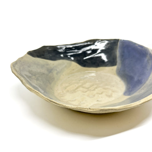 Handmade ceramic bowl with irregular edges and abstract glaze patterns in dark and light tones.