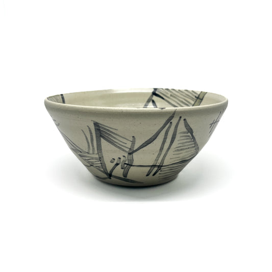 Handmade tea bowl with abstract, dark brushstroke designs on a textured surface.