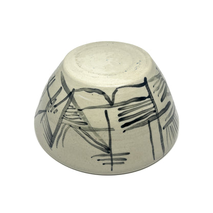 Bottom view of a textured ceramic tea bowl with abstract, dark painted lines and brushstrokes.