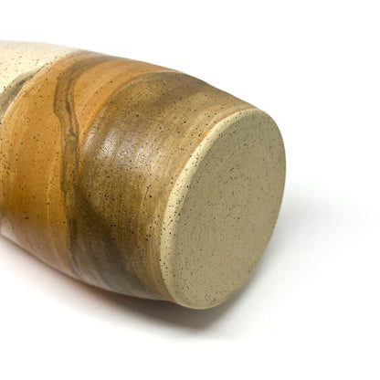 Angled view of the speckled bottom of a ceramic tumbler with flowing cream, gold, and brown glazes.