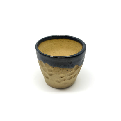 Small ceramic cup with a dark glazed rim over a textured, unglazed lower portion.