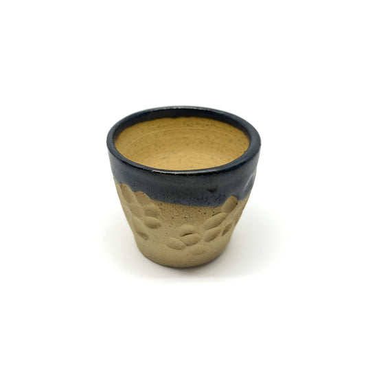Small ceramic cup with a dark glazed rim over a textured, unglazed lower portion.