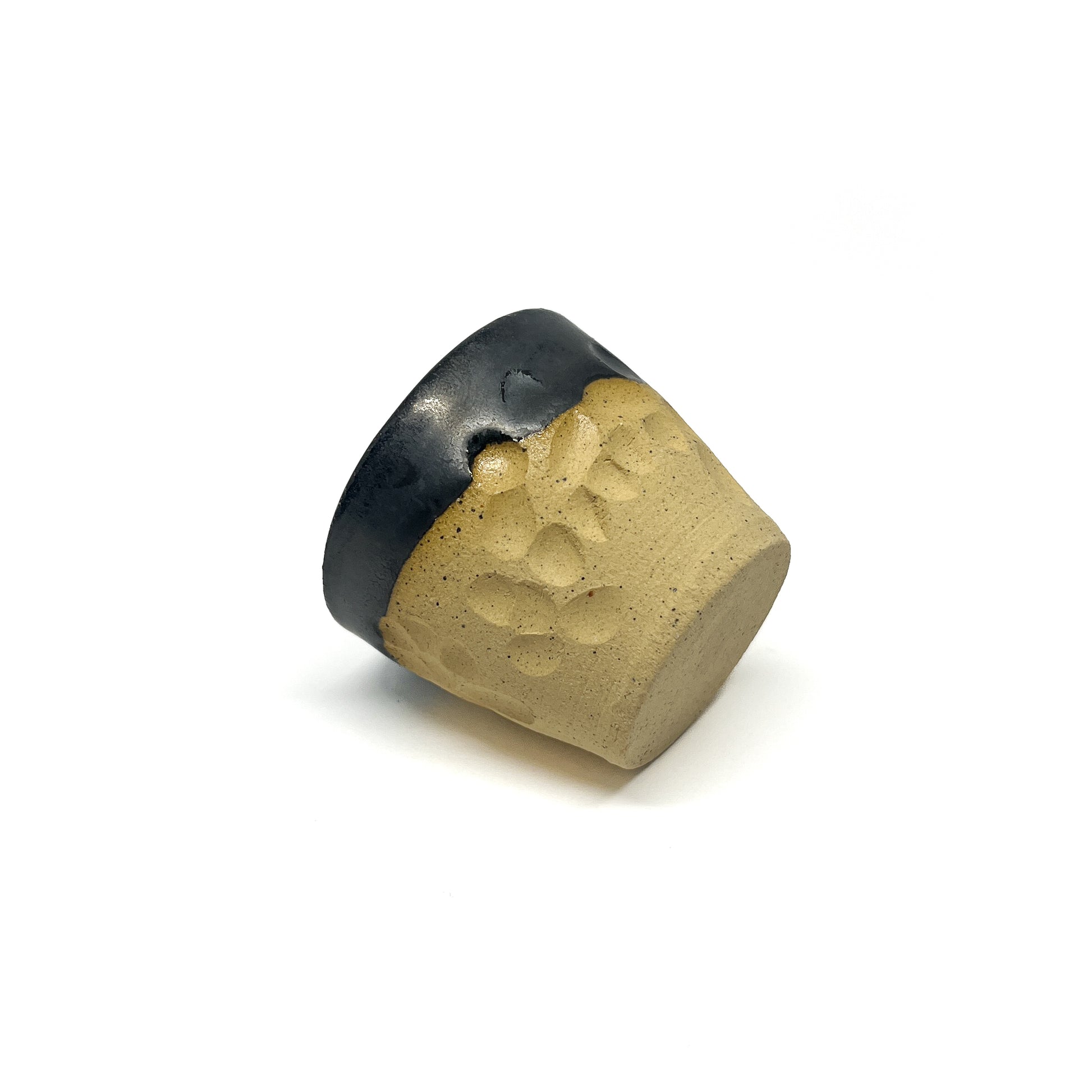 Tilted view of a small ceramic cup with a dark, glossy rim and a textured, matte body.