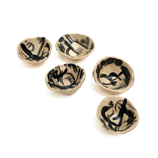 Five small, irregular ceramic pinch pots with abstract black brushstroke designs.