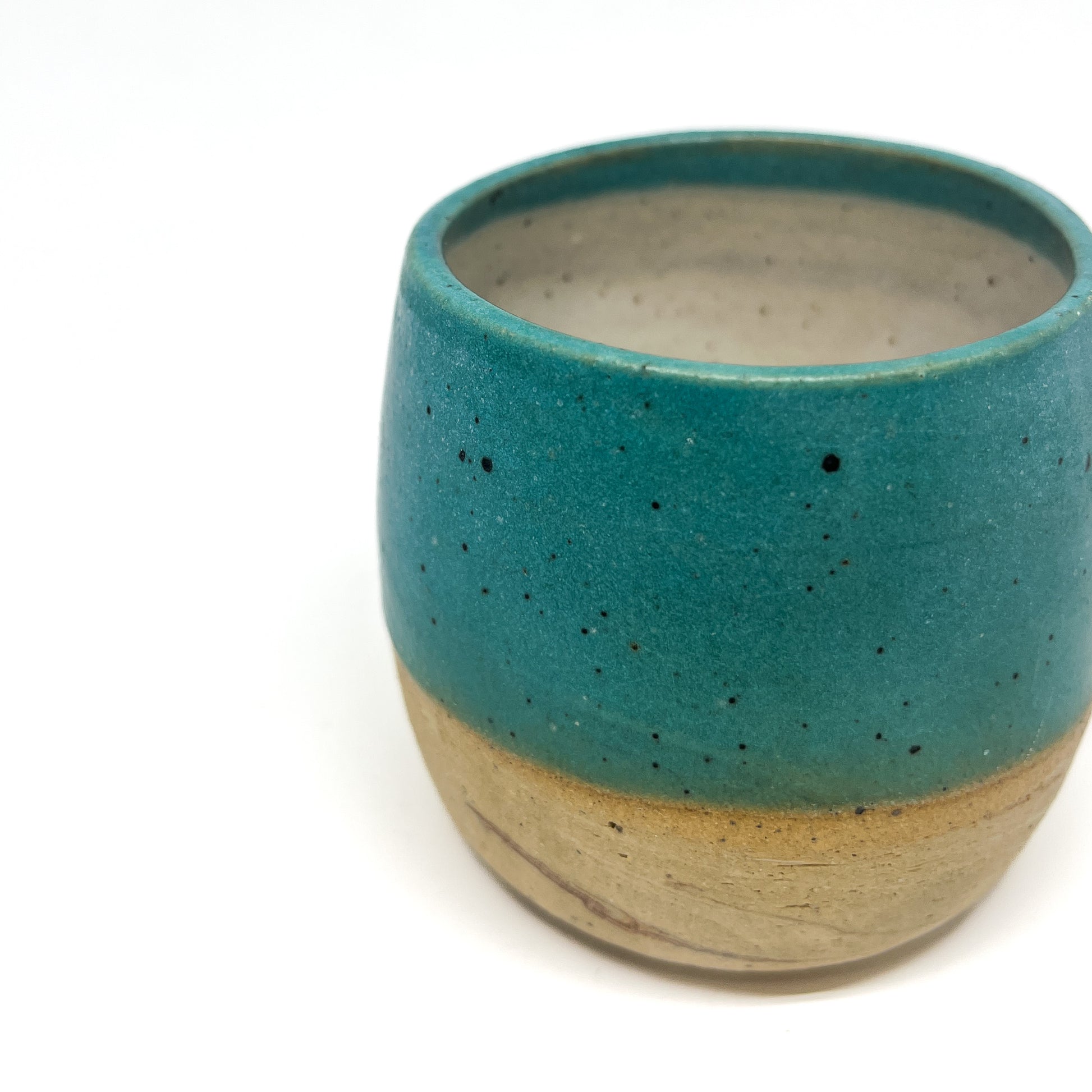 Close-up of a speckled ceramic cup with a teal glazed upper portion and a matte, unglazed base.