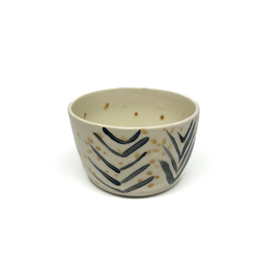 A small, round ceramic bowl features hand-painted black chevron patterns and scattered golden dots across its surface.