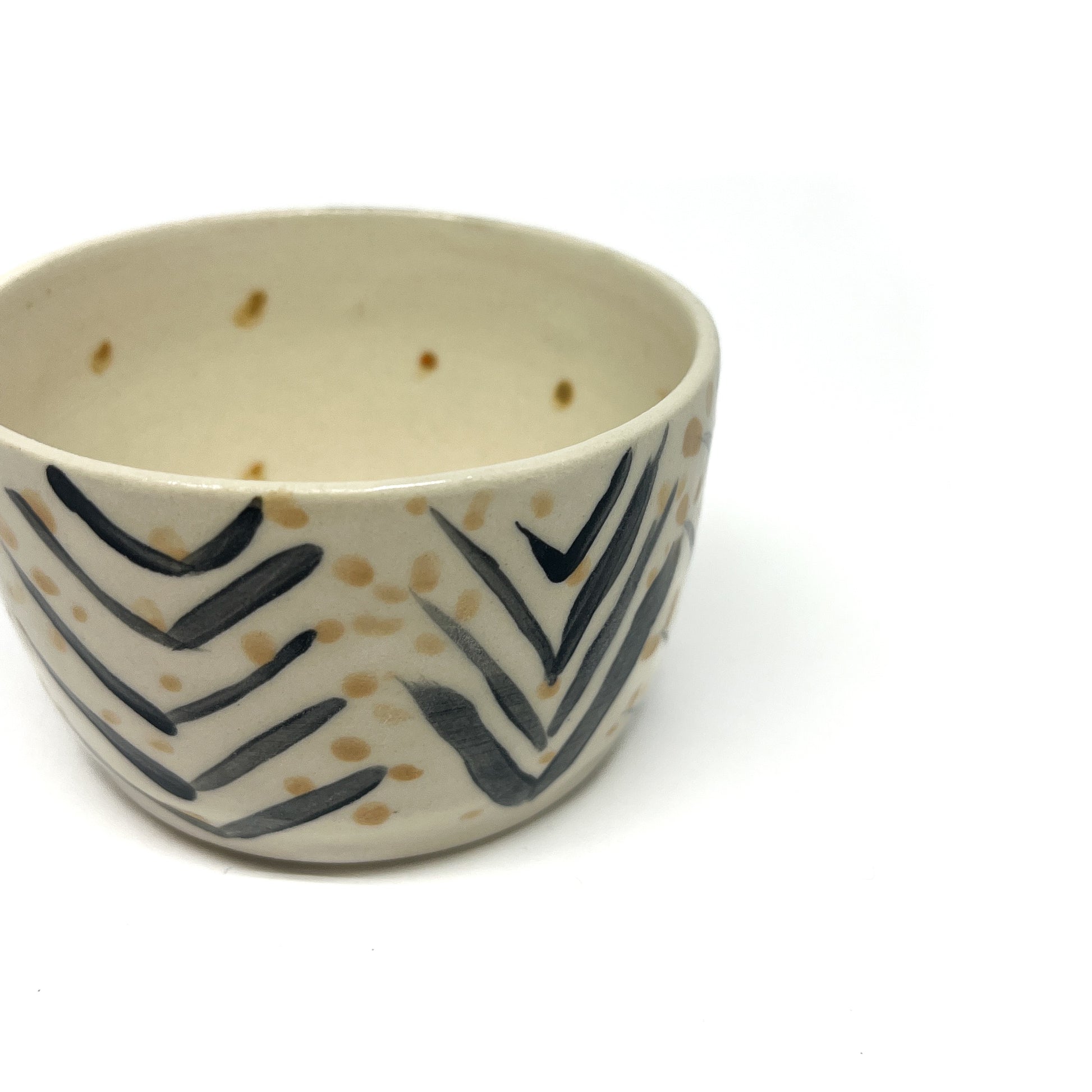 A close-up shows a small, round ceramic bowl adorned with bold black chevron designs and randomly placed golden dots.