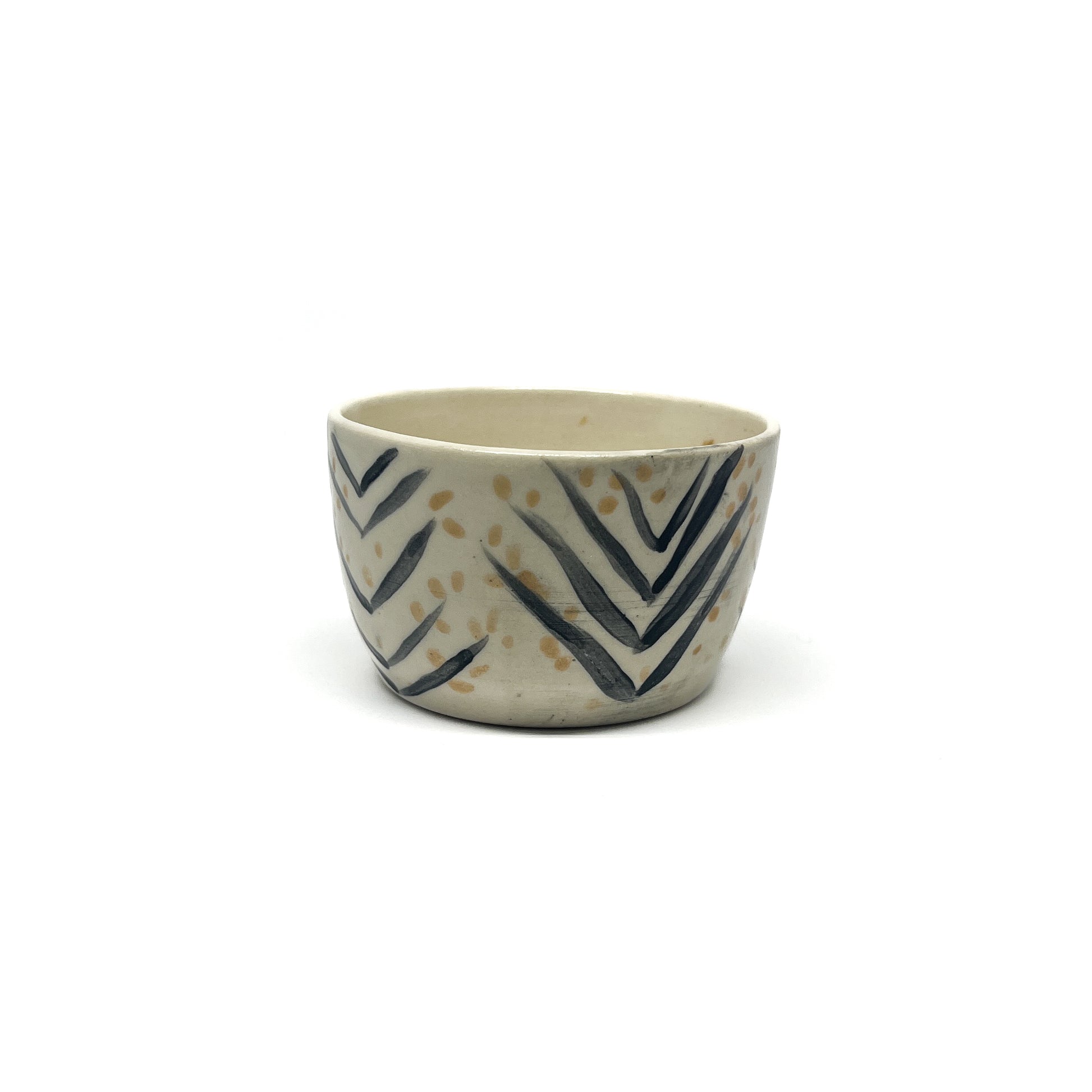 A small, round ceramic bowl features hand-painted black chevron patterns and scattered golden dots across its surface.