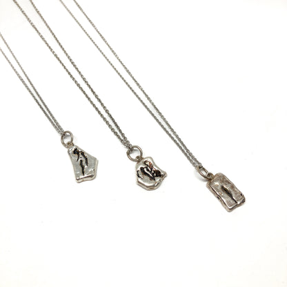Three small silver pendants with unique abstract designs on delicate chains.