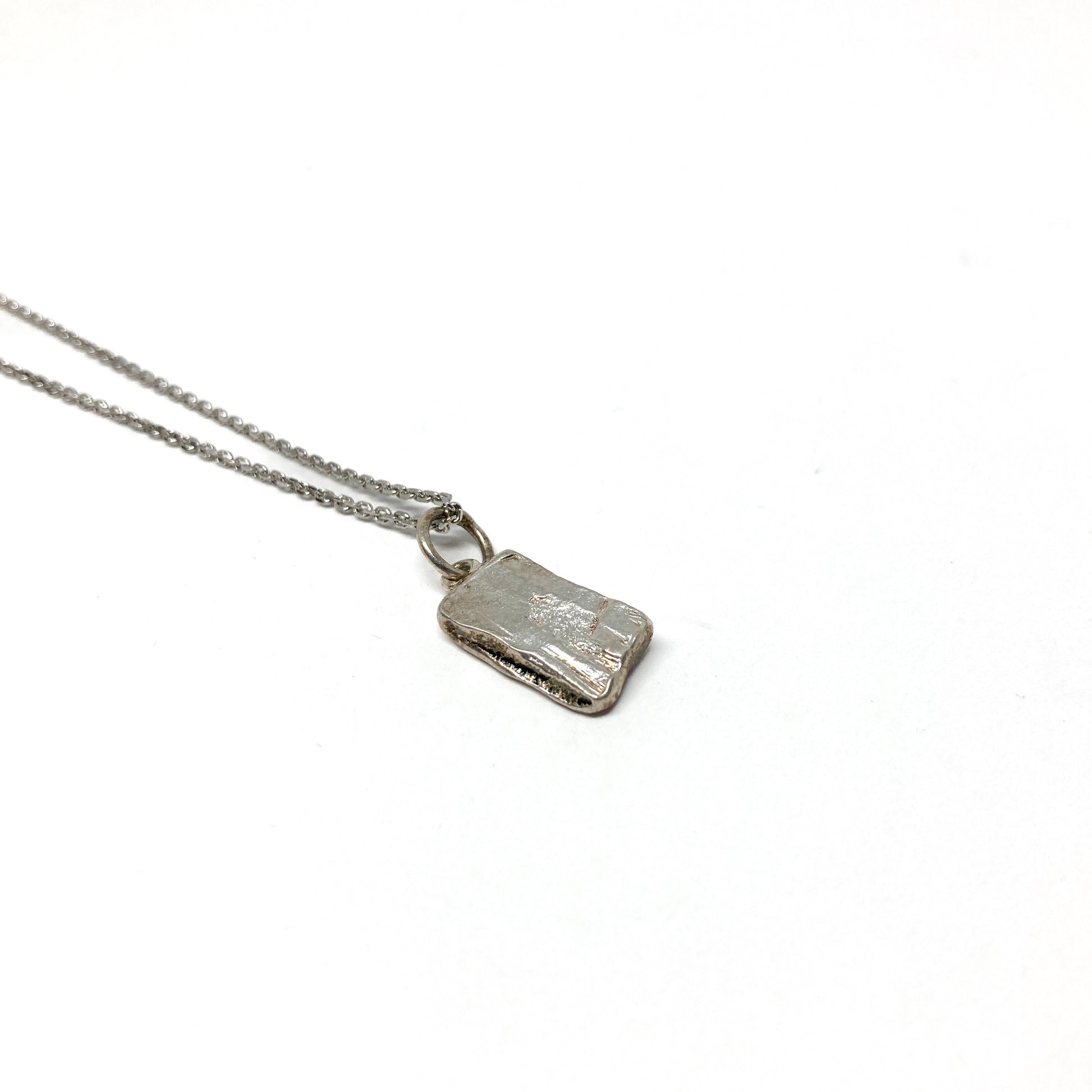 Back view of a small silver pendant revealing its smooth, unadorned surface.