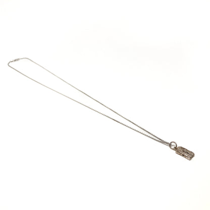 Angled view of a small silver pendant necklace lying on a plain surface.