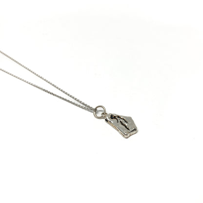 Close-up of a small silver pendant with a distinct abstract pattern and chain.
