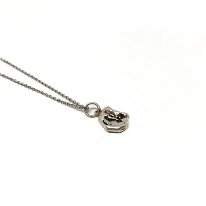 Detailed shot of a small, organically shaped silver pendant with dark accents.