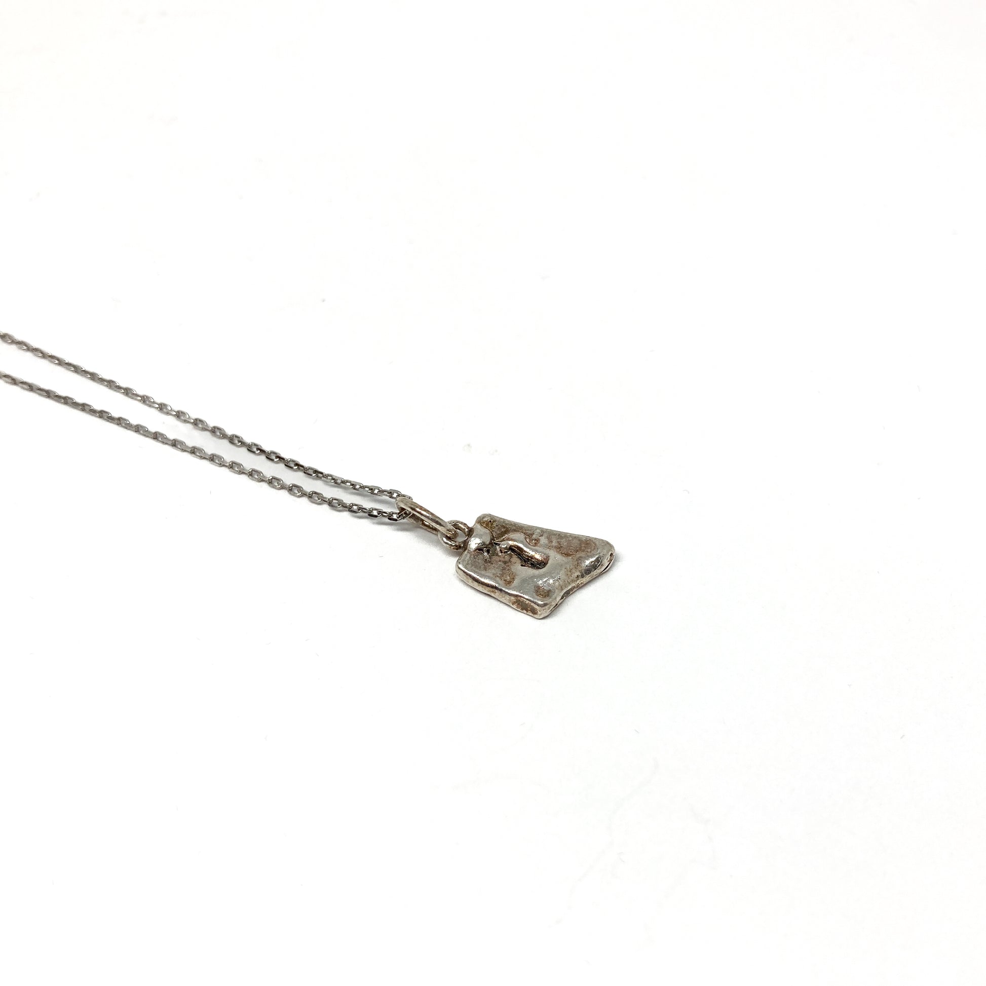 Angled close-up of a unique, small silver pendant.