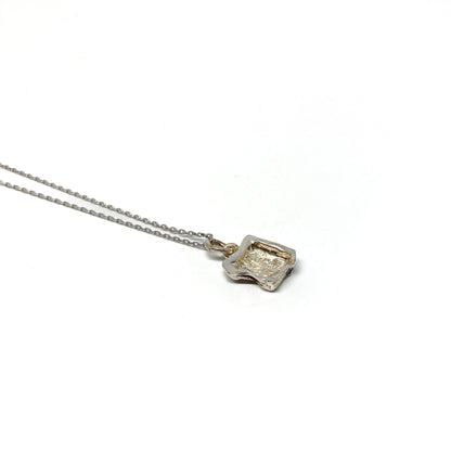 Back view of a small, irregularly shaped silver pendant.