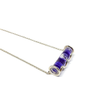 Silver necklace with a horizontal cylindrical glass pendant filled with swirling deep purple pigment and a visible air bubble.
