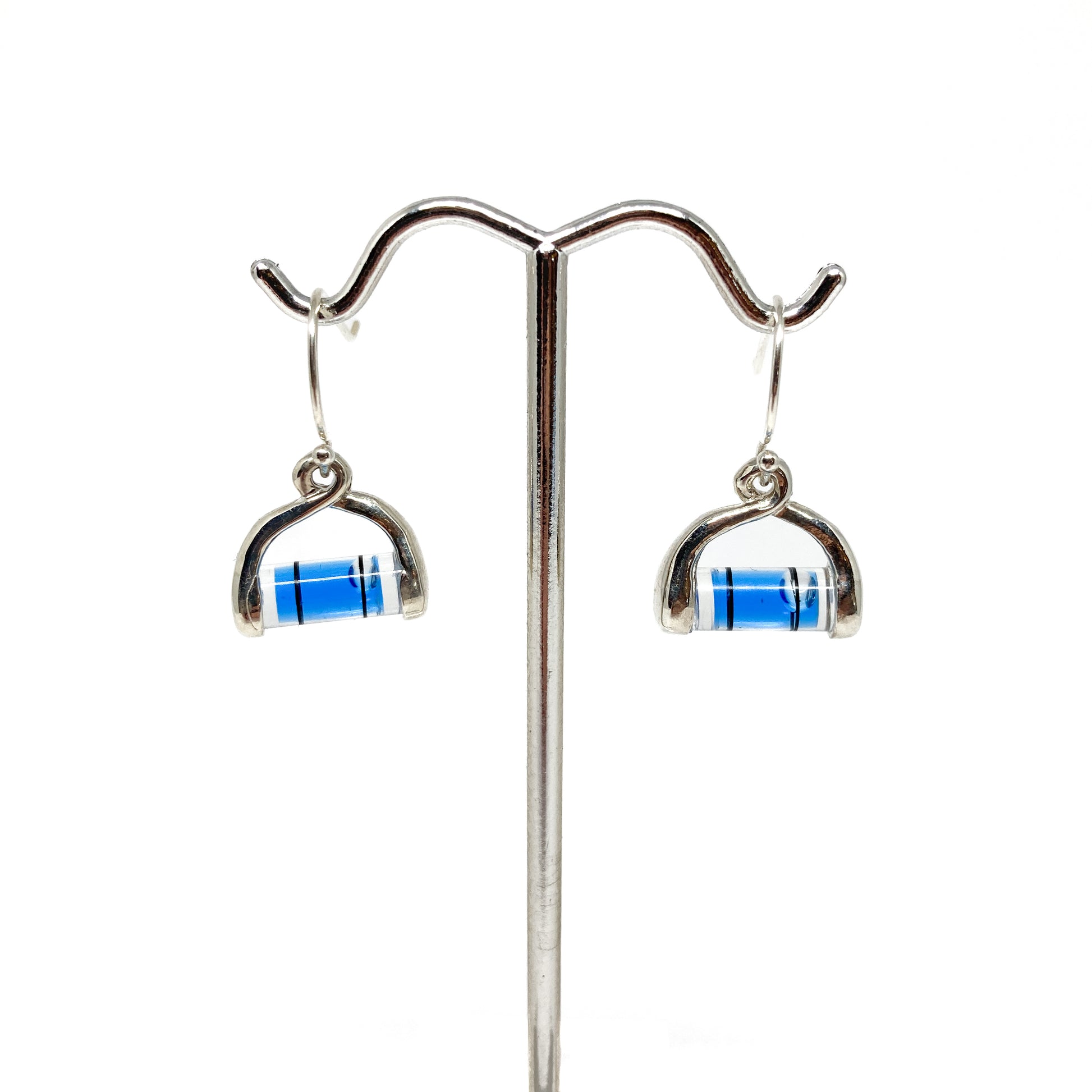Pair of silver bubble level earrings hanging from a silver display stand. Blue liquid and clear bubble visible.