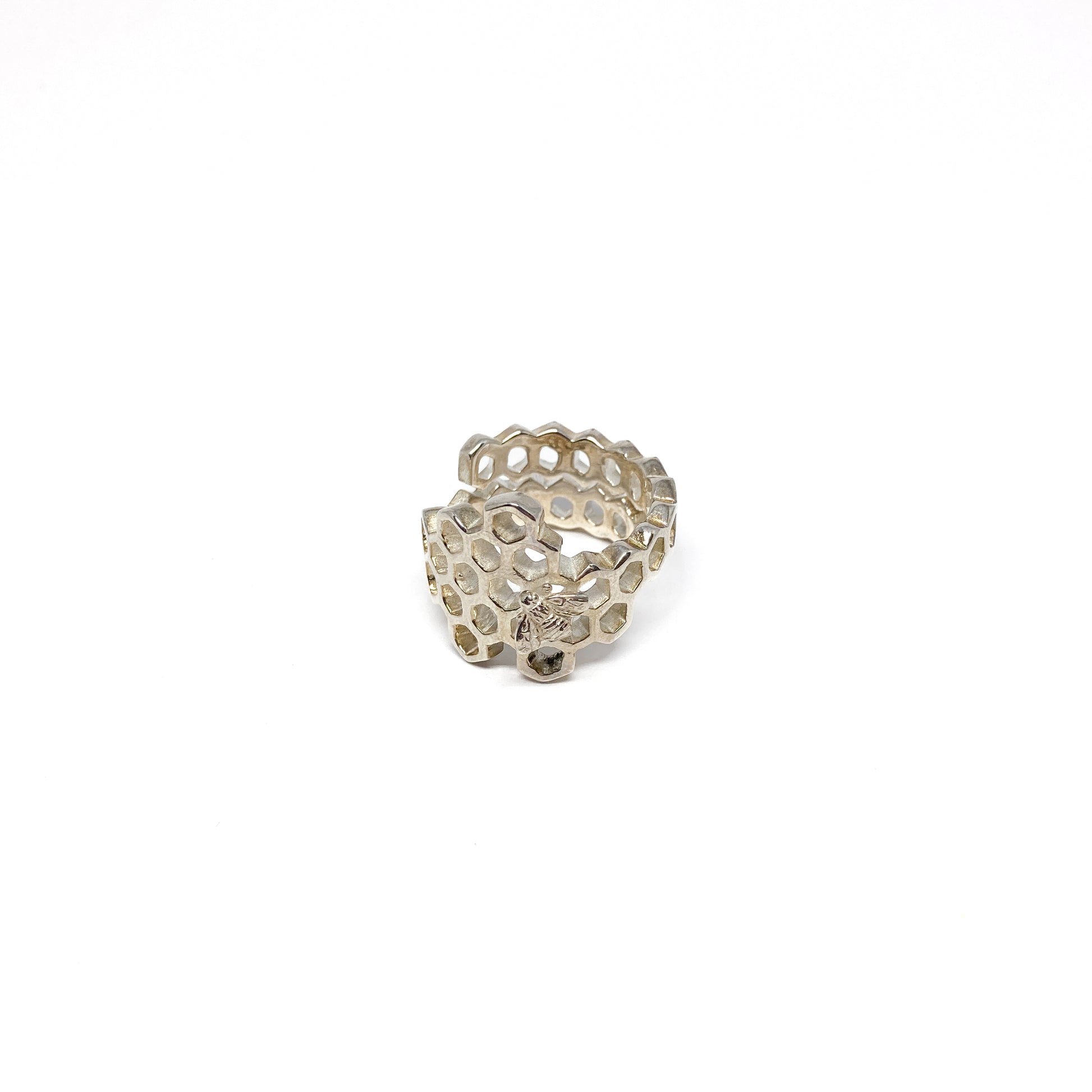 A shiny silver ring shaped like a honeycomb wraps around, featuring a detailed bee on one cell.