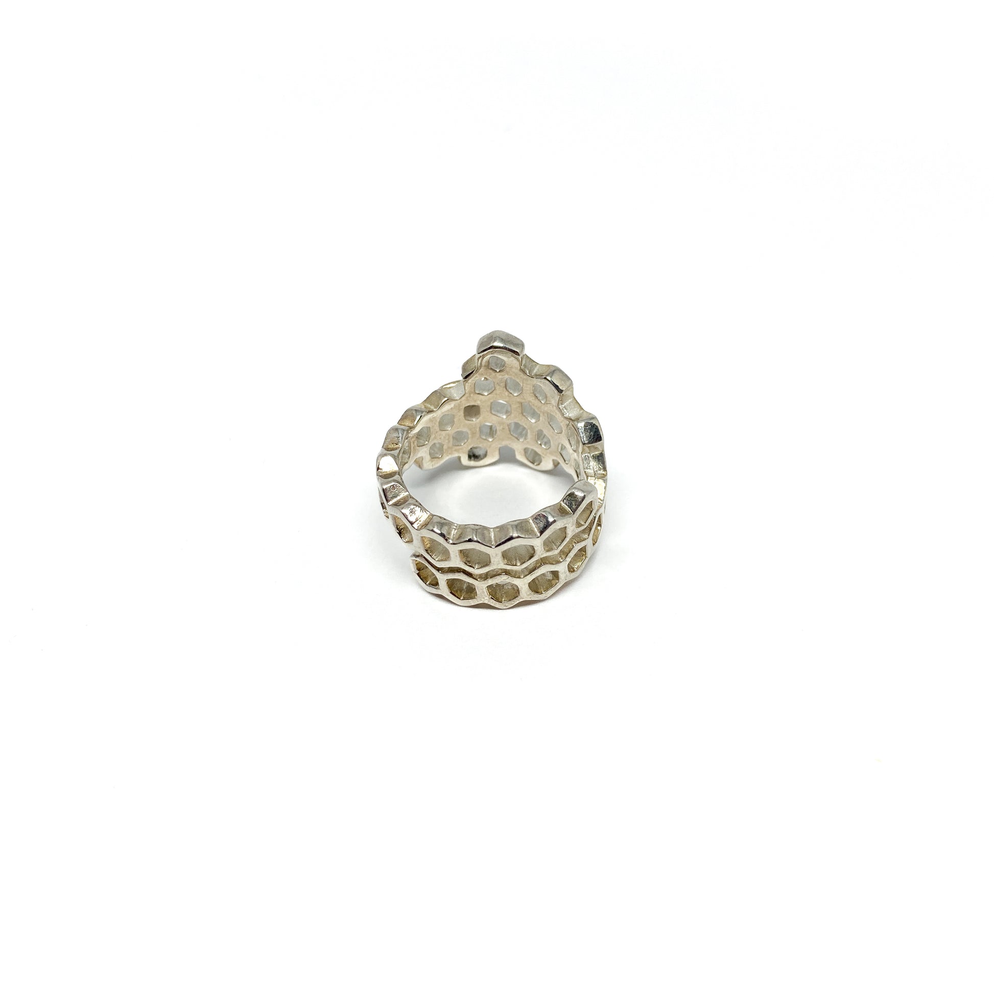 A shiny silver ring shaped like a honeycomb is viewed from the back, showing its intricate hexagonal cells.