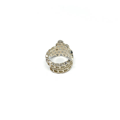 A shiny silver ring shaped like a honeycomb is viewed from the back, showing its intricate hexagonal cells.