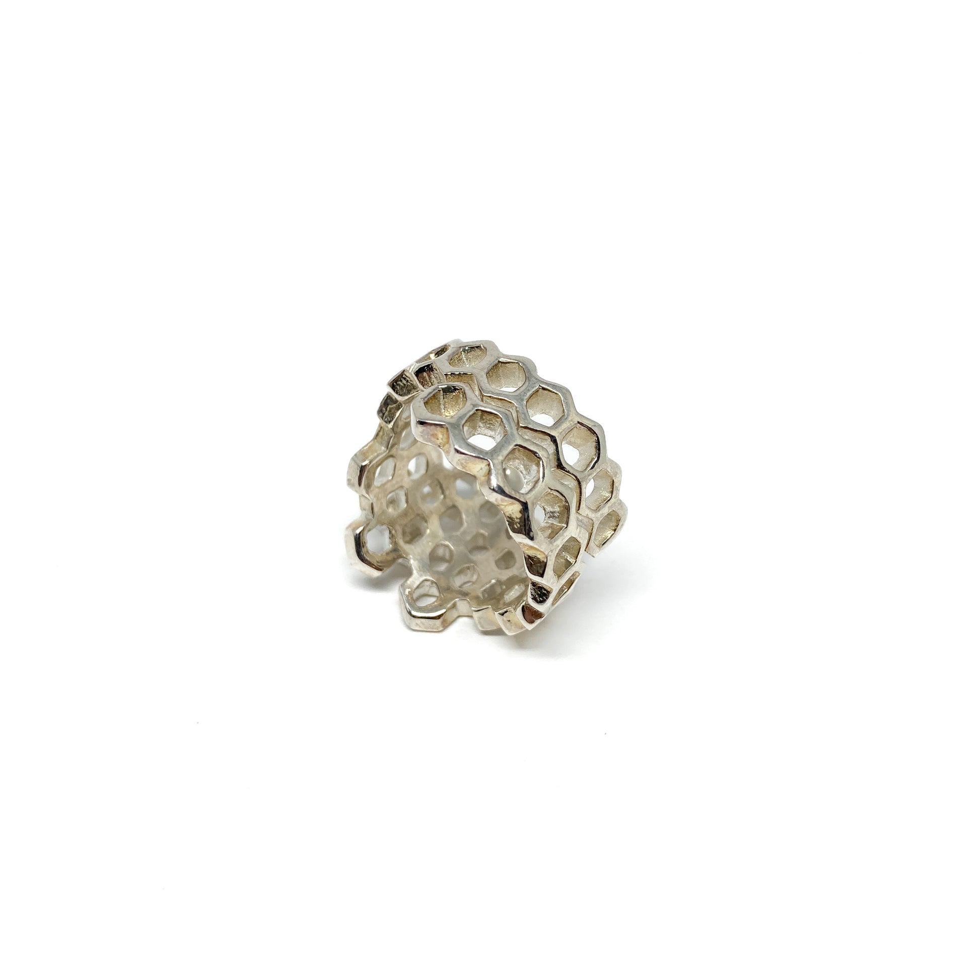 A shiny silver ring with an openwork honeycomb design is shown in a close-up view.