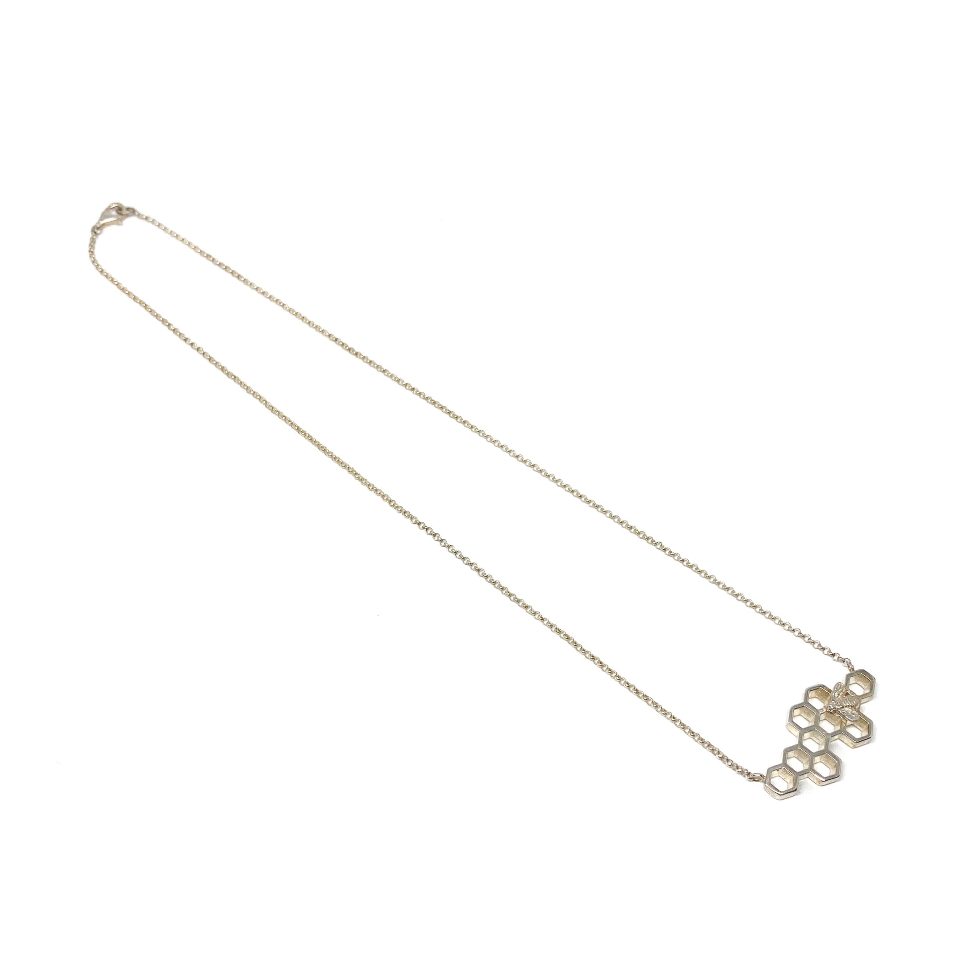 A long, delicate silver chain leads to a honeycomb pendant with a bee detail at the bottom right.