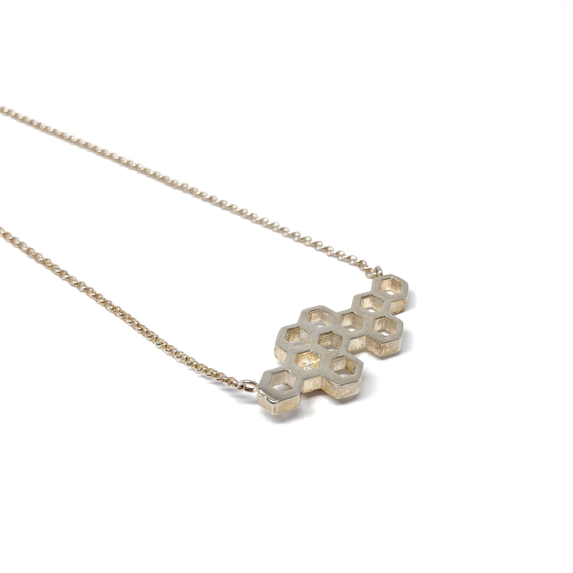 A silver necklace features a horizontal honeycomb pendant made of interconnected hexagonal shapes.