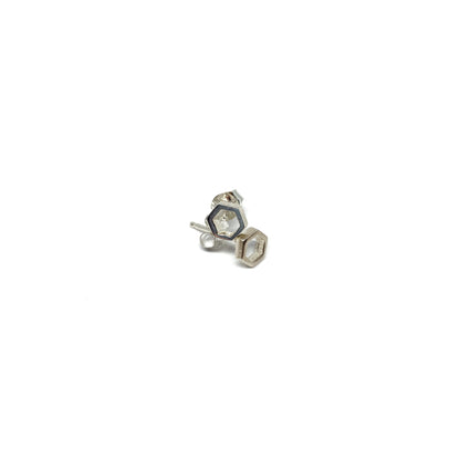 A pair of shiny silver stud earrings, each featuring a small, open hexagonal design, are shown close-up.