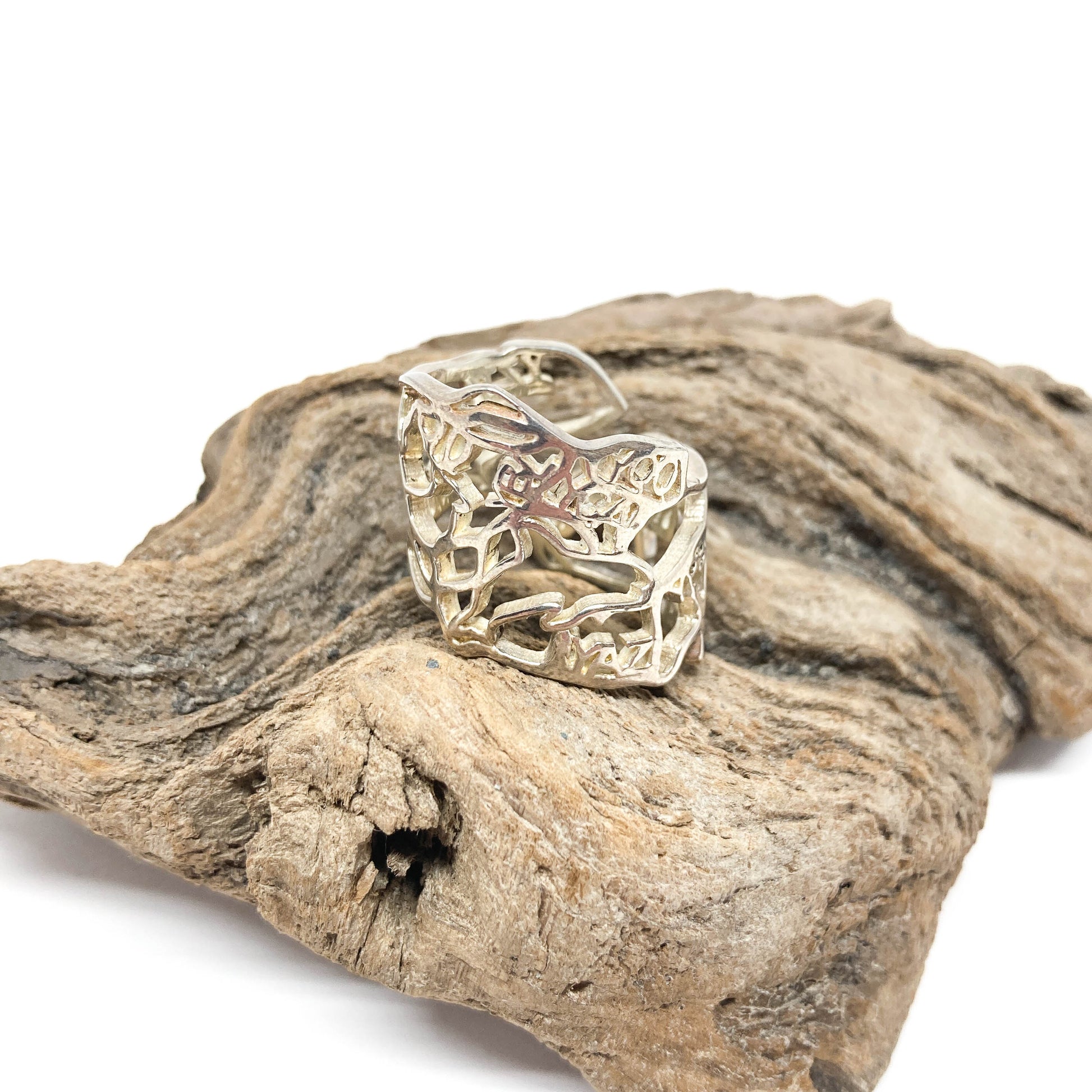 A shiny silver ring with a cut-out design of Canada rests on a textured piece of driftwood.