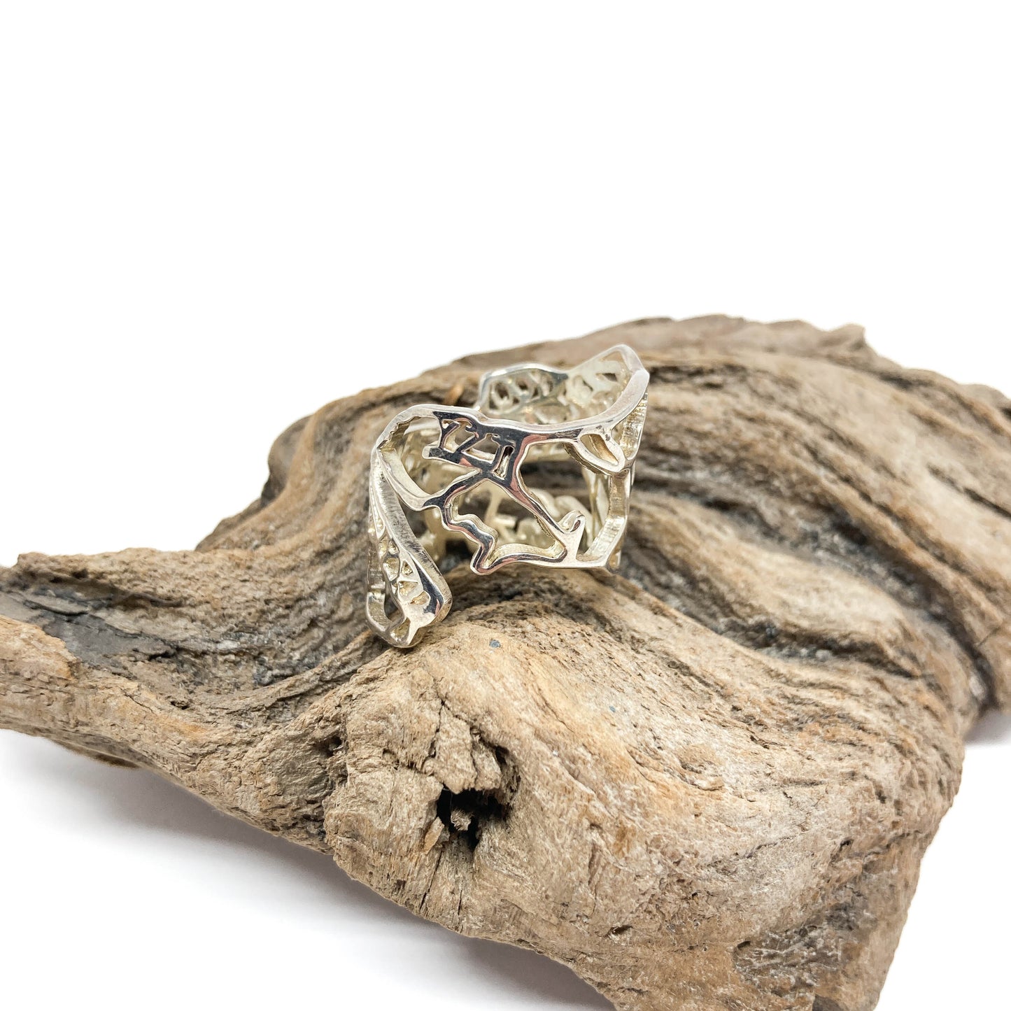 A shiny silver ring with a cut-out design of the map of Canada rests on a textured piece of driftwood.