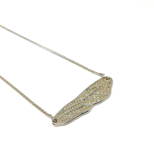 A delicate silver necklace features a horizontal pendant shaped like a detailed dragonfly wing.