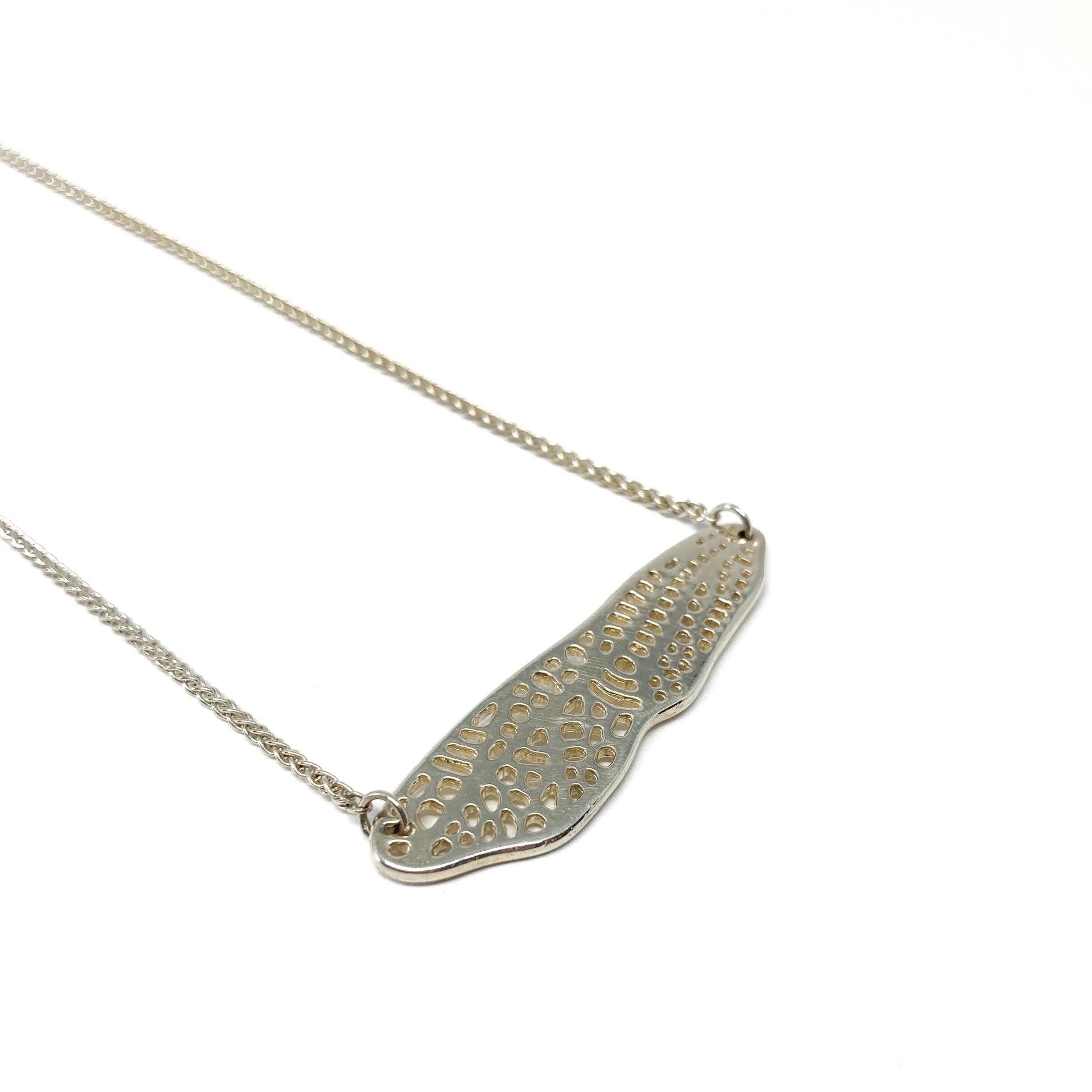 A delicate silver necklace features a horizontal pendant shaped like a detailed dragonfly wing.