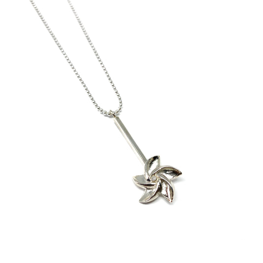 A silver ball chain necklace features a pendant with a bar and a stylized, swirling floral or pinwheel design.