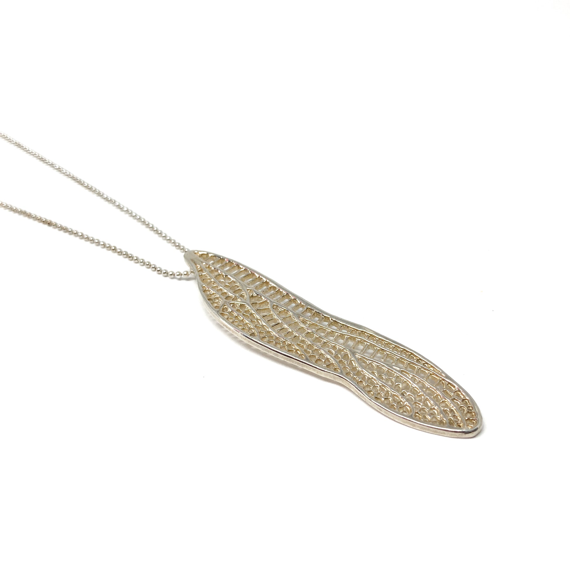 A silver ball chain necklace features a delicate, openwork pendant shaped like a dragonfly wing.