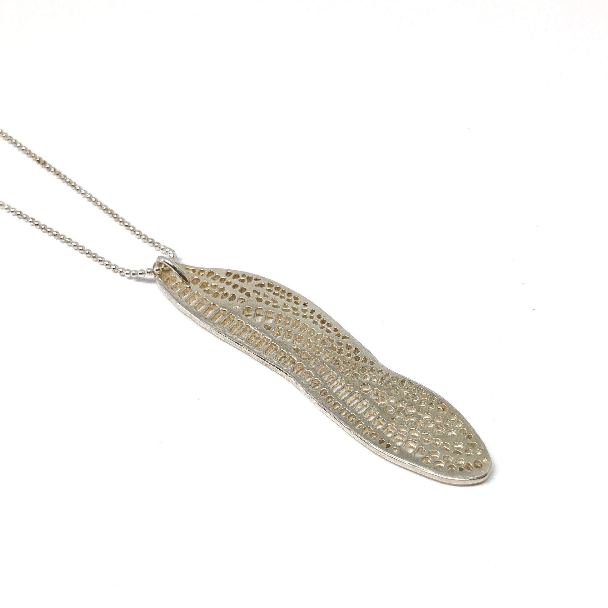 A silver ball chain necklace features a long, slender pendant with an intricate, openwork dragonfly wing design.