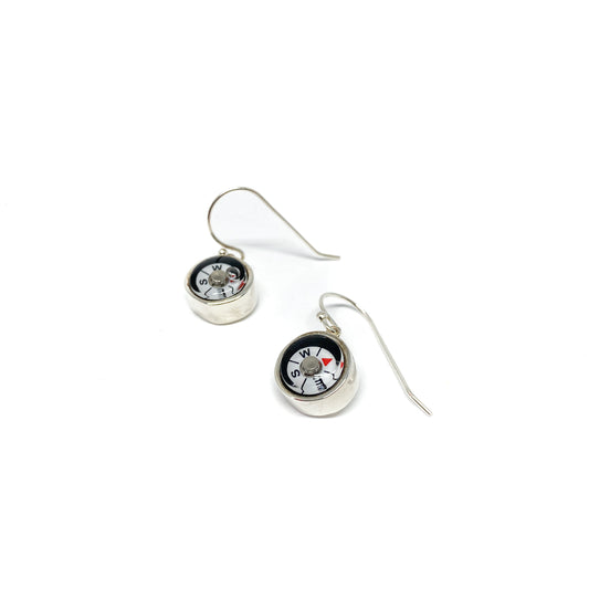 Two shiny silver dangle earrings feature miniature compasses with visible north, south, east, and west markings.