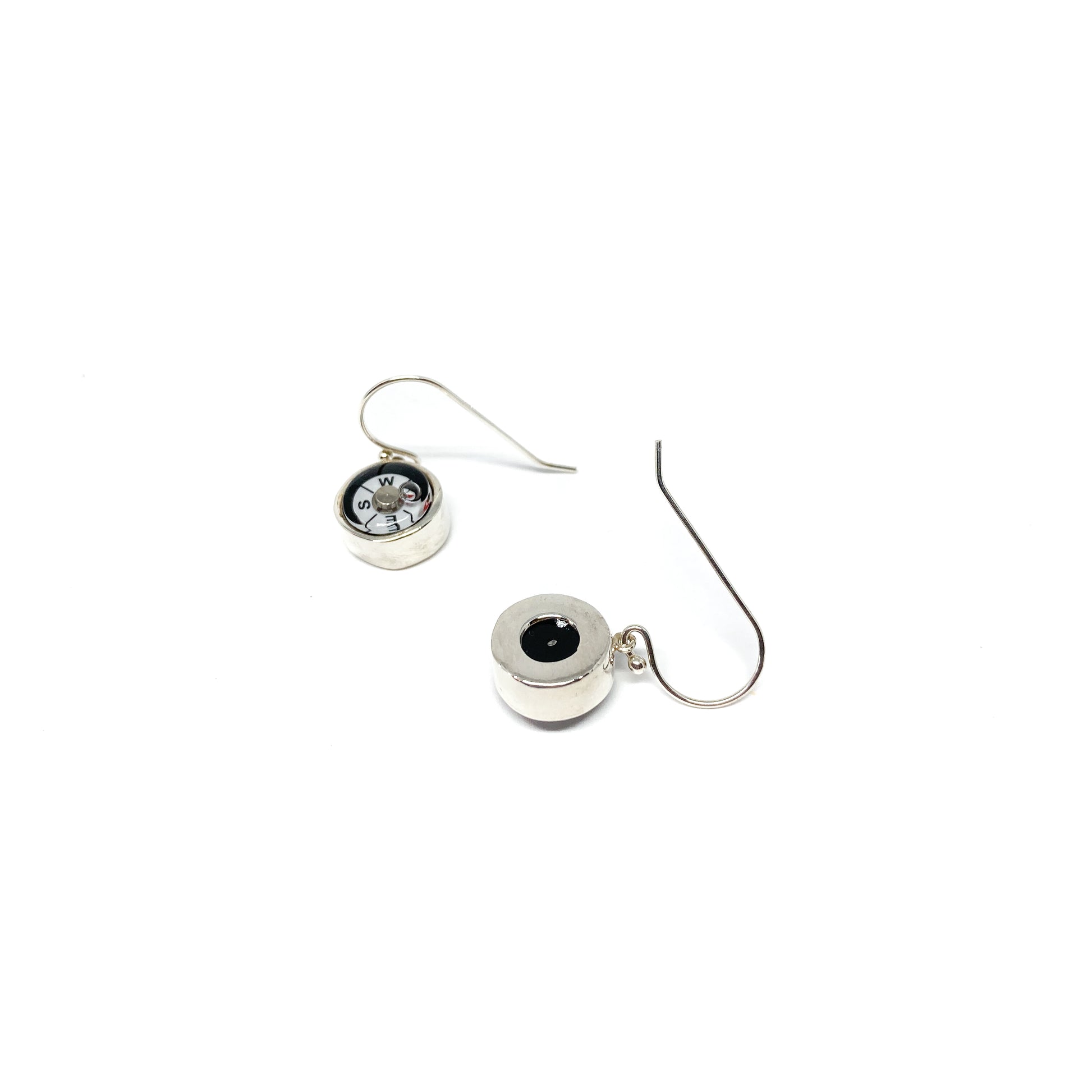 Two shiny silver dangle earrings feature miniature compasses; one shows the back with a dark center.